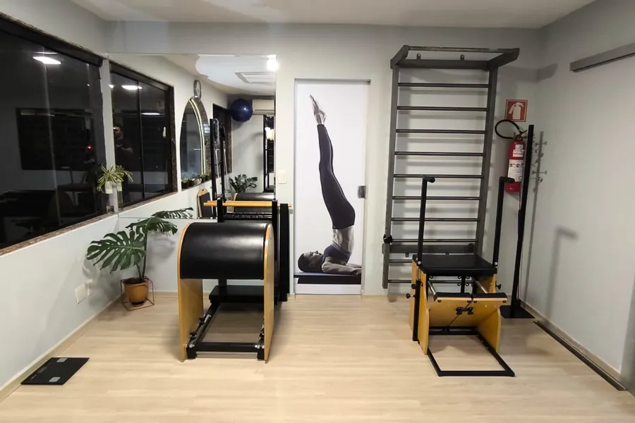 A sala do estúdio vista da entrada: janela, espelho, barrel, a porta com o painel de pilates, o espaldar e a chair, sem ninguém.